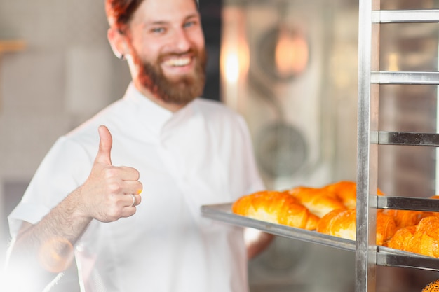 Ein junger hübscher Bäcker zeigt seinen Daumen