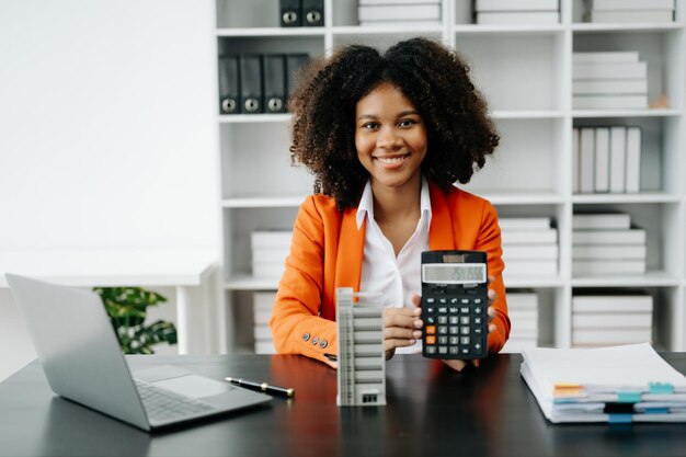 Foto ein junger immobilienmakler arbeitet mit laptop und tablet am tisch in einem modernen büro und einem kleinen haus daneben