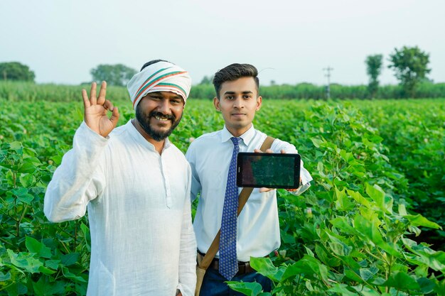 Ein junger indischer Agronom zeigt einem Landwirt auf einem Tablett einige Informationen auf dem Landwirtschaftsfeld