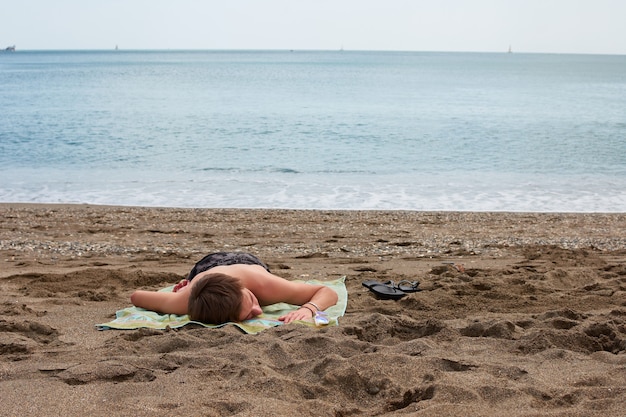 Ein junger kaukasischer Mann, der auf einem Handtuch am Strand liegt