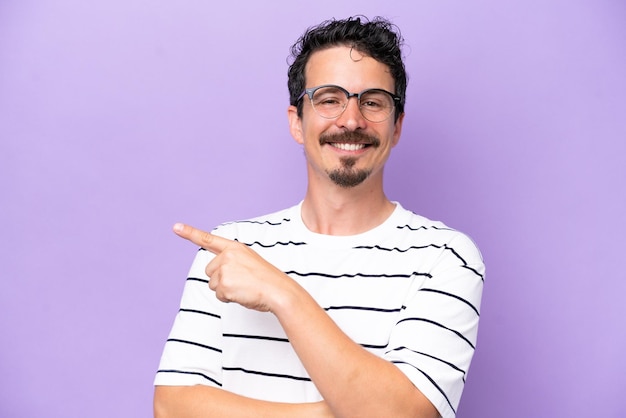 Ein junger kaukasischer Mann, isoliert auf lila Hintergrund, mit Brille und Zeigeseite.