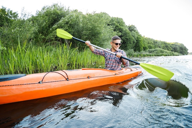 Ein junger kaukasischer Mann sitzt in einem Kajak und paddelt Das Konzept der Wasserunterhaltung