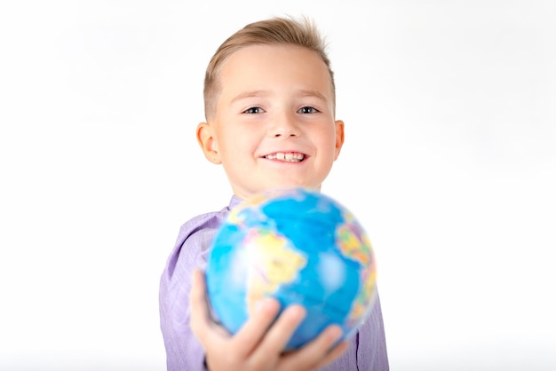 Ein junger kaukasischer Schuljunge zeigt vor sich einen Globus auf weißem Studio-Hintergrund