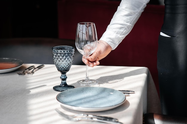 Ein junger Kellner in einer stilvollen Uniform ist damit beschäftigt, den Tisch in einem schönen Gourmet-Restaurant in der Nähe zu servieren Tischservice im Restaurant