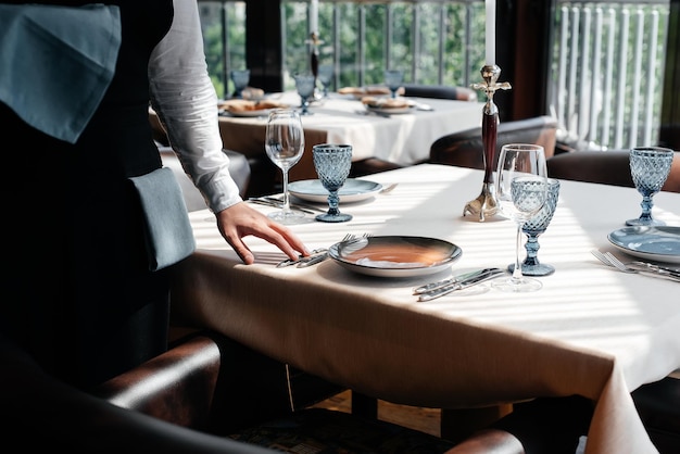 Foto ein junger kellner in einer stilvollen uniform ist damit beschäftigt, den tisch in einem schönen gourmet-restaurant in der nähe zu servieren tischservice im restaurant