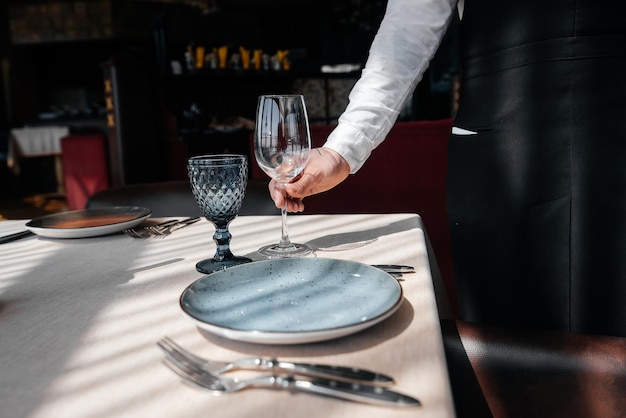 Ein junger Kellner in einer stilvollen Uniform ist damit beschäftigt, den Tisch in einem schönen Gourmet-Restaurant in der Nähe zu servieren Tischservice im Restaurant