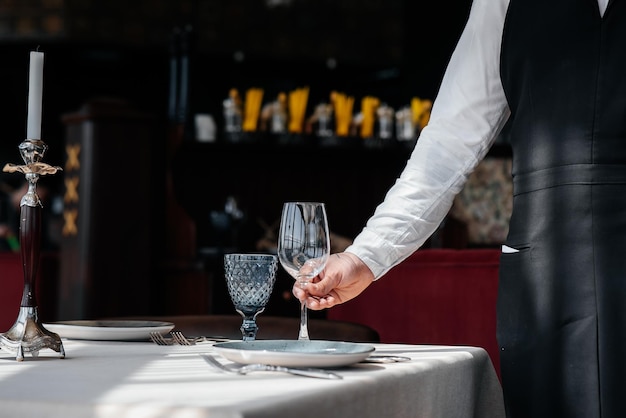 Ein junger Kellner in einer stilvollen Uniform ist damit beschäftigt, den Tisch in einem schönen Gourmet-Restaurant in der Nähe zu servieren Tischservice im Restaurant