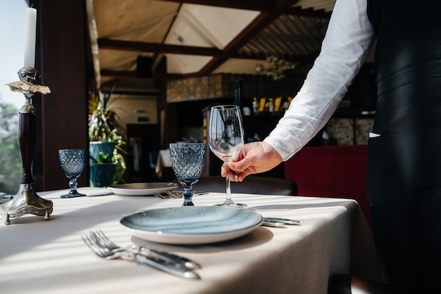 Ein junger Kellner in stilvoller Uniform ist damit beschäftigt, den Tisch in einem schönen Gourmetrestaurant aus nächster Nähe zu servieren. Restauranttätigkeit auf höchstem Niveau.