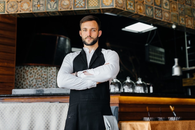 Ein junger Kellner mit Bart zieht sich eine Schürze um und bereitet sich auf einen Arbeitstag in einem feinen Restaurant vor.