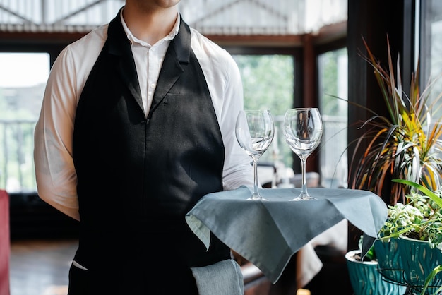 Ein junger Kellner steht mit Weingläsern in einem stilvollen modernen Restaurant Tischservice im Restaurant Haute Cuisine Service und Wartung Nahaufnahme