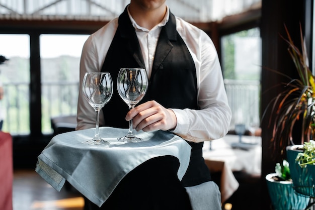 Ein junger Kellner steht mit Weingläsern in einem stilvollen modernen Restaurant Tischservice im Restaurant Haute Cuisine Service und Wartung Nahaufnahme