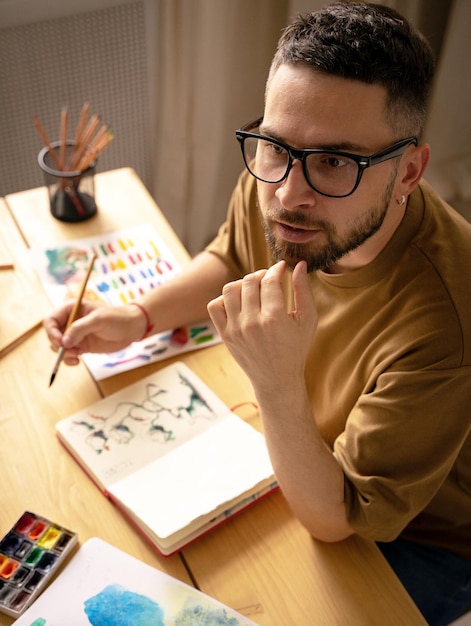 Ein junger Künstler macht eine Skizze mit einem Pinsel an seinem Schreibtisch Porträt eines kreativen Menschen in seinem Atelier Leben im kreativen Atelier Der Prozess der Schaffung eines Kunstwerks die Suche nach Inspiration