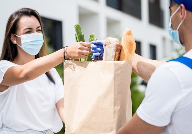 Ein junger Kurier, der eine Schutzmaske und Handschuhe trägt, liefert während der Quarantäne Waren an eine junge Frau