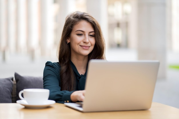 Ein junger Lehrer unterrichtet aus der Ferne online auf einem Laptop, der allein in einem Sommercafé sitzt