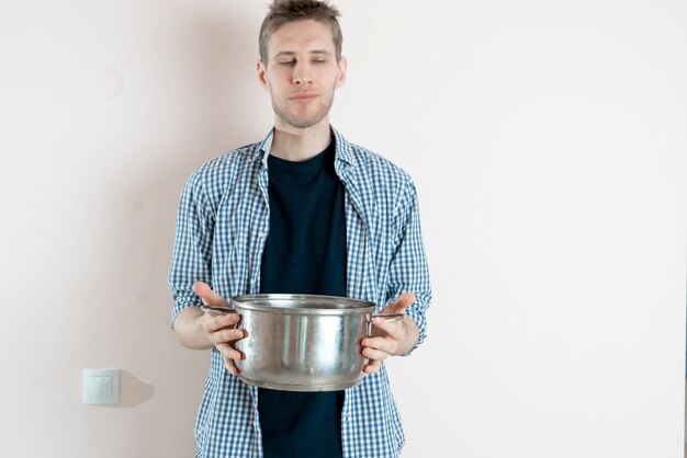 Ein junger männlicher Koch, der einen Topf mit darin zubereiteter Suppe hält und isoliert an der Wand steht