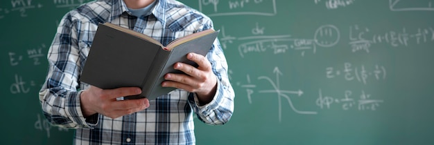 Ein junger männlicher Professor an der Universität, der ein Buch im Klassenzimmer hält