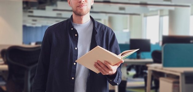 Ein junger männlicher Professor an der Universität, der ein Buch im Klassenzimmer hält