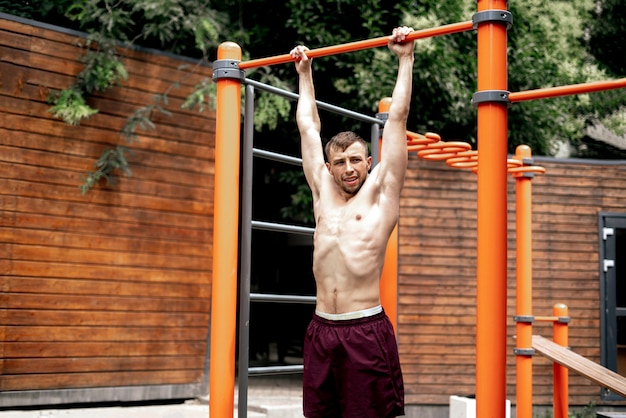 Ein junger männlicher Sportler macht Klimmzüge auf dem Street-Workout-Spielplatz