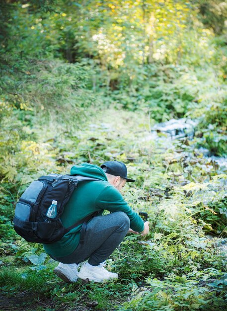 Ein junger männlicher Tourist fotografiert in einem Wald mit einer Smartphone-Kamera. Tourismus, aktiver Lebensstil