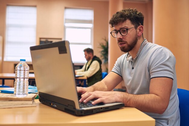 Ein junger Mann arbeitet mit seinem Laptop in der Bibliothek