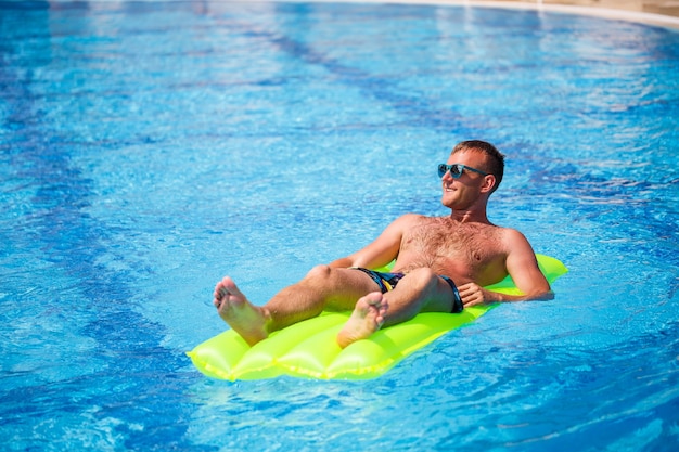 Ein junger Mann badet im Pool auf einer gelben Luftmatratze