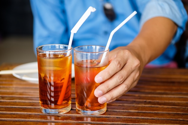 Ein junger Mann benutzt ein Stroh, um von einer Glashand des grünen Tees auf hölzerner Tabelle zu trinken