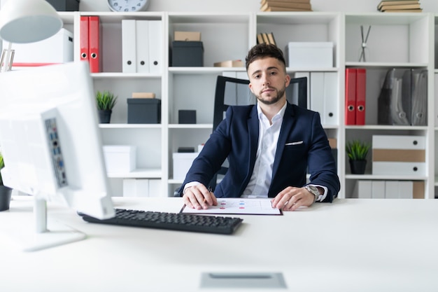 Ein junger Mann, der im Büro an einem Computertisch sitzt und mit Dokumenten arbeitet.