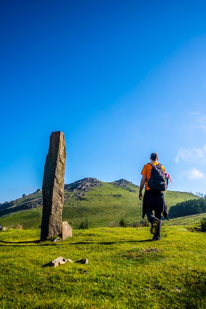 Ein junger Mann, der neben einem prähistorischen Dolmen auf dem Monte Adarra in Urnieta in der Nähe von San Sebastian geht. Gipuzkoa, Baskenland, vertikales Foto