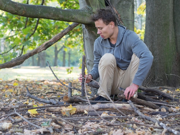 Ein junger Mann, der sich im Wald hockte und einen Stock in der Hand hielt