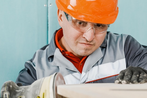 Ein junger Mann, ein Zimmermann, poliert ein Holzbrett mit einem Orbitalschleifer Das Konzept von Bau und Reparatur