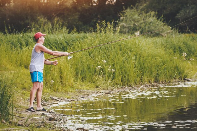 Ein junger Mann fischt an der Küste eines Süßwassersees, der von einer üppigen Landschaft gesäumt ist.