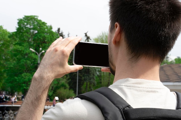 Ein junger Mann fotografiert mit seinem Handy im Park