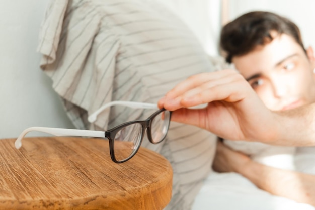 Ein junger Mann greift nach seiner Brille, nachdem er im Bett aus einem Traum aufgewacht ist