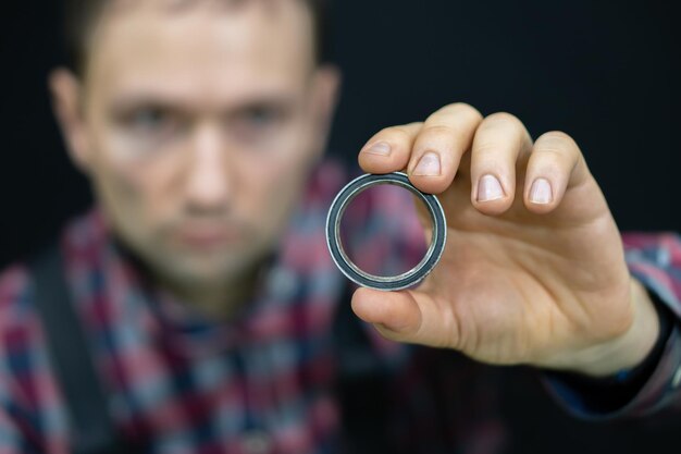 Foto ein junger mann hält auf schwarzem hintergrund ein lager in der hand ein fahrradmechaniker in der werkstatt wechselt die lager für die lenksäule reparatur von motorrädern und autos im servicecenter