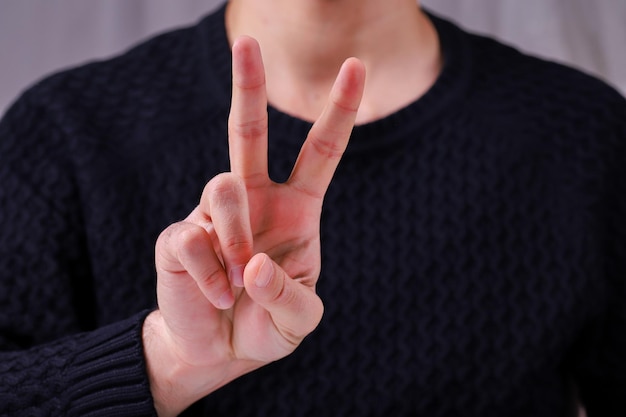 Foto ein junger mann hält zwei finger hoch und zeigt ein friedens- oder siegessymbol und den buchstaben v in der gebärdensprache