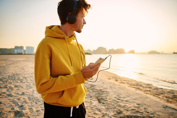 Foto ein junger mann hört während des sonnenuntergangs musik am strand gegen den himmel