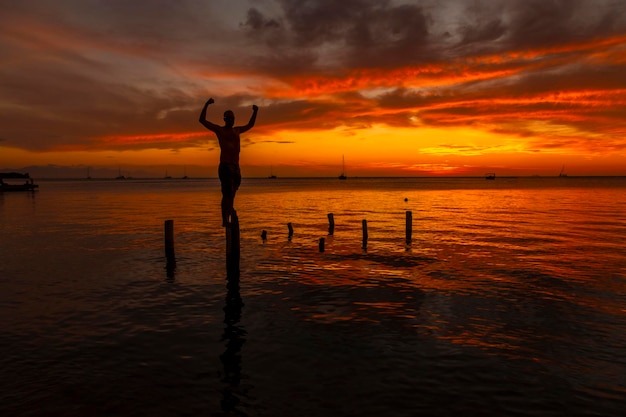 Ein junger Mann im Wasser am Orange Sunset am Strand von West End von Roatan, Honduras