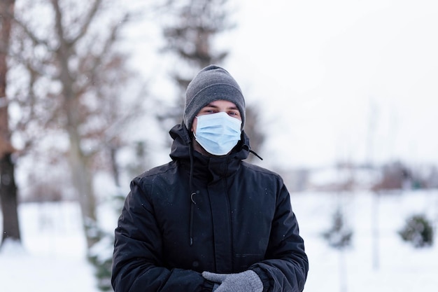 Ein junger Mann im Winter trägt eine Maske Junger Mann in antiviraler Schutzmaske auf der Straße Der Mann in Winterkleidung in einer Schutzmaske Junger Mann in warmer Kleidung und Schal an einem Wintertag