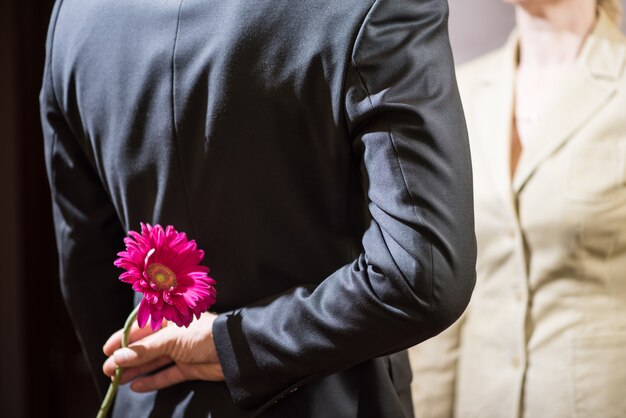 Ein junger Mann in einem Anzug hält eine Gerbera-Blume hinter seinem Rücken