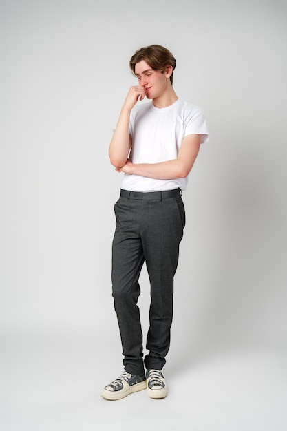 Ein junger Mann in einem beiläufigen weißen T-Shirt und grauen Hose denkt über einen einfachen Hintergrund nach