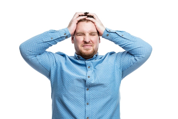 Ein junger Mann in einem blauen Hemd hält seinen Kopf in Unmut Negative Emotionen und Stress isoliert auf weißem Hintergrund