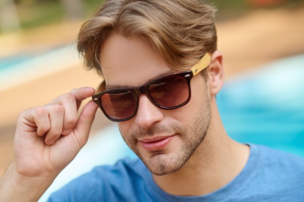 Ein junger Mann in einem blauen T-Shirt und einer Sonnenbrille, der selbstbewusst aussieht