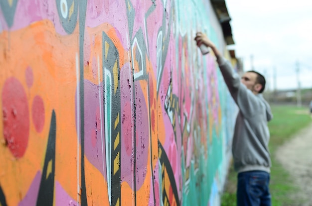 Ein junger Mann in einem grauen Hoodie malt Graffiti in Pink und Grün