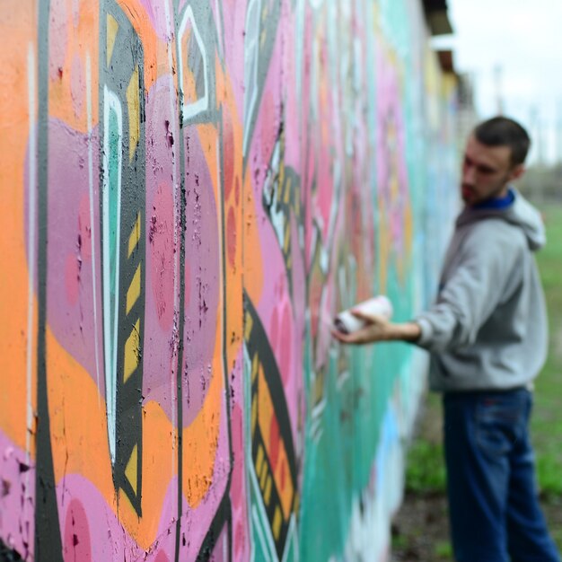 Ein junger Mann in einem grauen Hoodie malt Graffiti in rosa und grünem c