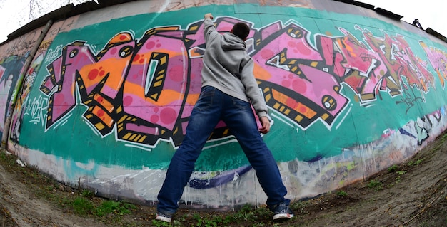 Ein junger Mann in einem grauen Hoodie malt Graffiti in rosa und grünem c