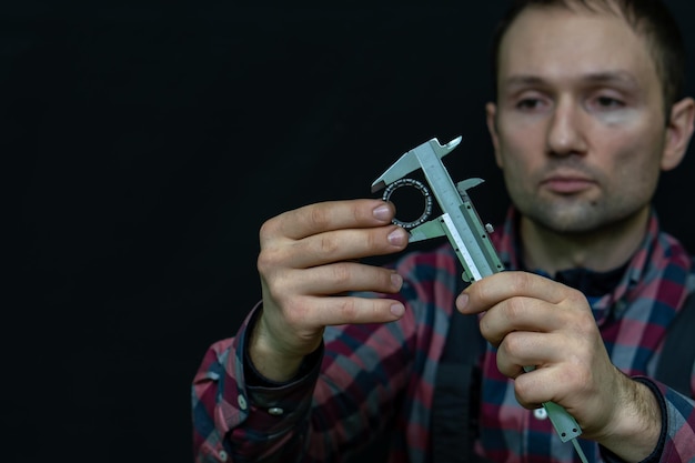 Ein junger Mann in einem Hemd und mit einem Messgerät in den Händen Bremssattel in den Händen eines Mechanikers auf schwarzem Hintergrund Arbeiter hält während der Arbeit Lagerwerkzeuge