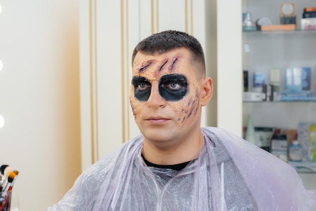 Ein junger Mann in einem schönen gruseligen Make-up in Form eines Totenkopfes für den Halloween-Urlaub in der Studio-Nahaufnahme. Glückliches Halloween-Konzept.