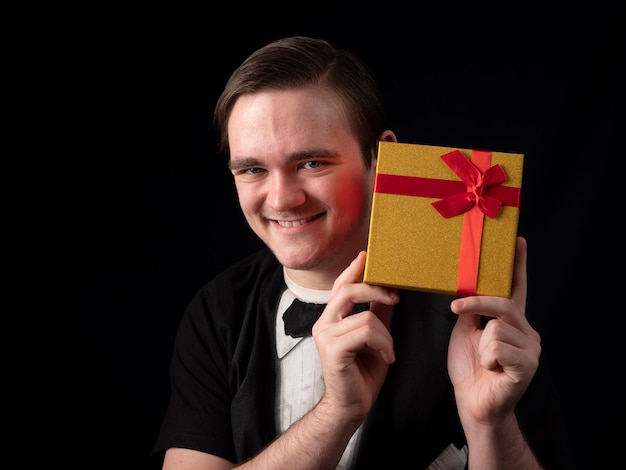 Ein junger Mann in einem schwarzen T-Shirt-Anzug hält ein gelbes Geschenk in der Hand auf einem schwarzen