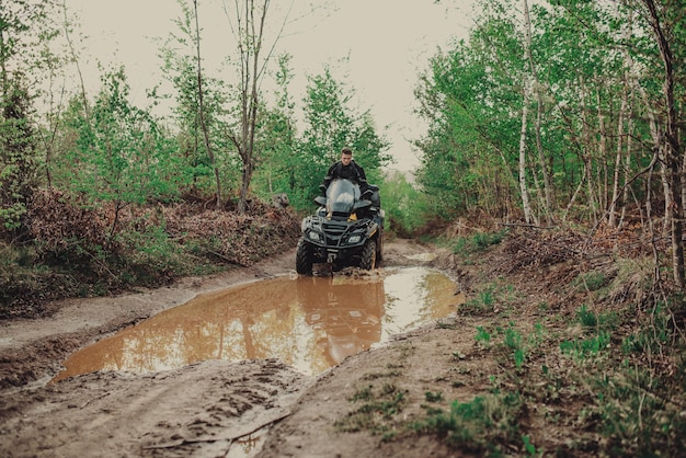 Foto ein junger mann in einem weißen helm fährt auf einem quad-bike durch den wald. extremes hobby. ein ausflug zum atv auf der straße von baumstämmen