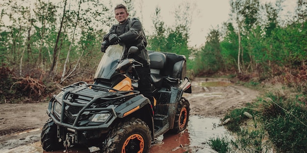 Ein junger Mann in einem weißen Helm fährt auf einem Quad-Bike durch den Wald. Extremes Hobby. Ein Ausflug zum ATV auf der Straße von Baumstämmen